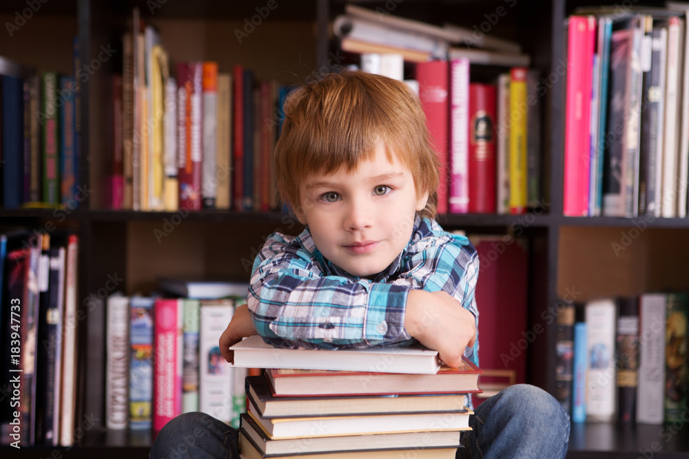 preschooler little boy reading a book in the library. the little boy with books near a bookcase

