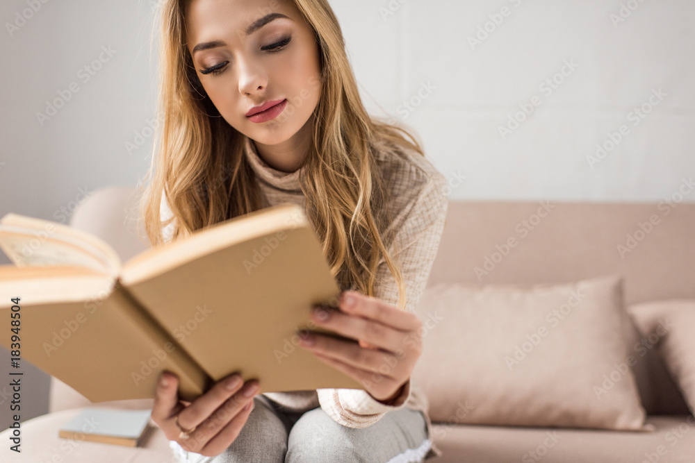 attractive young woman reading book on cozy couch at home attractive young woman reading book on cozy couch at home