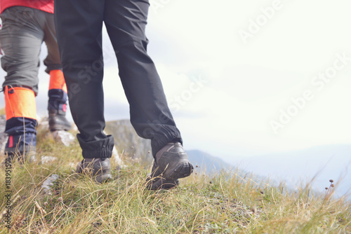 Close-up of legs of young hikers walking on the country path. Young couple trail waking. Focus on hiking shoes