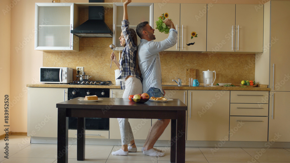 Attractive young joyful couple have fun dancing and singing while cooking in the kitchen at home Attractive young joyful couple have fun dancing and singing while cooking in the kitchen at home