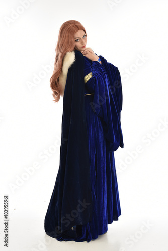  full length portrait of girl wearing long blue velvet gown and fur lined cloak, standing pose  on white background.