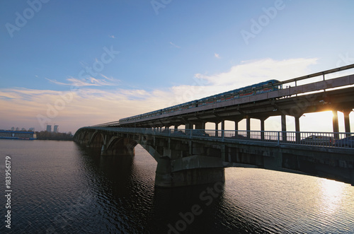 Picturesque view over the Metro (Subway) Bridge over the Dnipro river in Kyiv, Ukraine. Metro train are moving along the bridge. Sunrise at winter morning