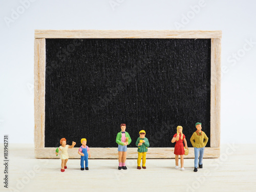 Miniature children standing in front of a blackboard on wooden background. Back to school concept.