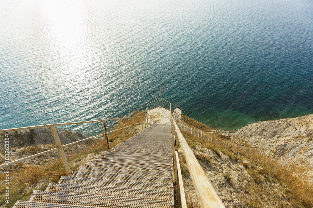 Obraz premium A steep descent down the long metal stairs to the shore of the blue sea