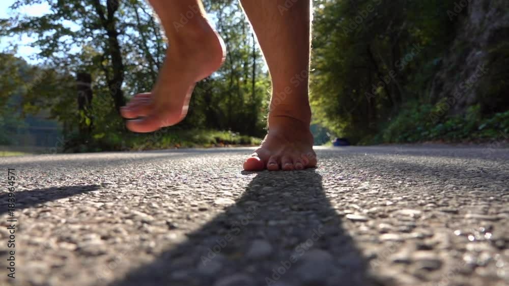 SLOW MOTION, LENS FLARE Unknown barefoot man running alone through autumn forest on idyllic afternoon. Young male jogger in blue boardshorts running barefoot towards and past camera lens on sunny day.