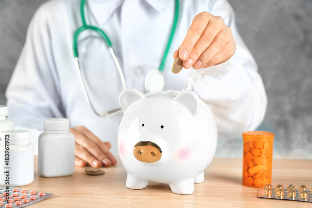 Doctor putting coin into piggy bank. Health care concept Doctor putting coin into piggy bank. Health care concept