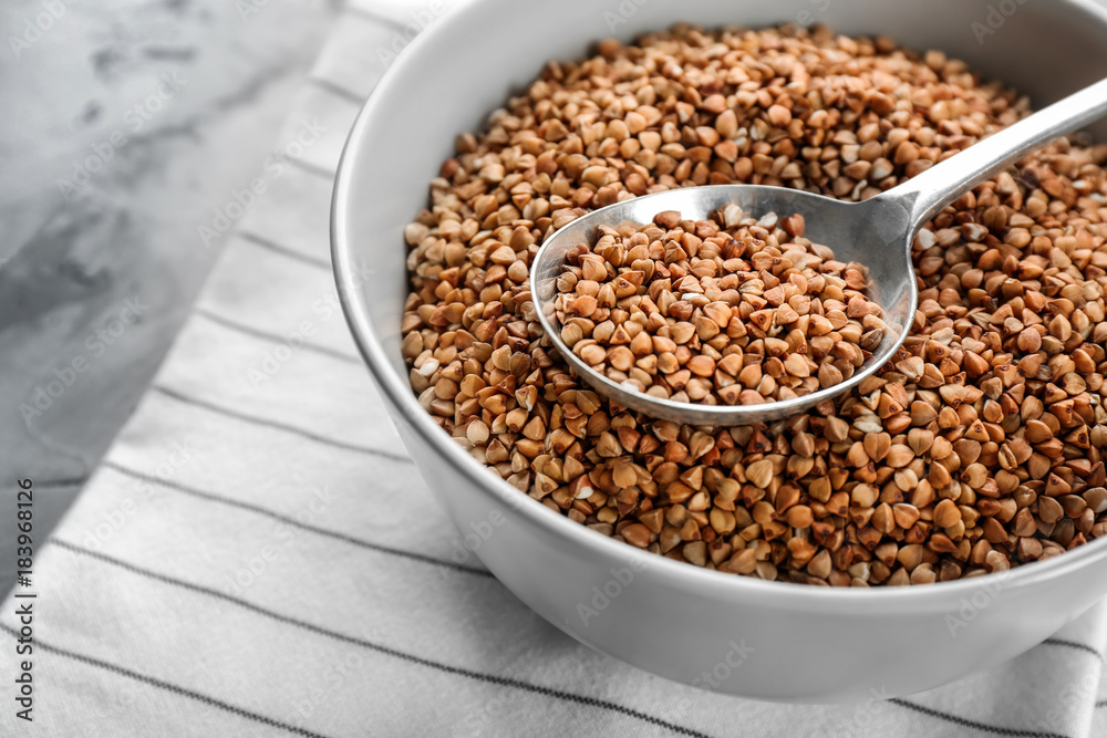 Bowl and spoon with raw buckwheat and spoon on table Bowl and spoon with raw buckwheat and spoon on table