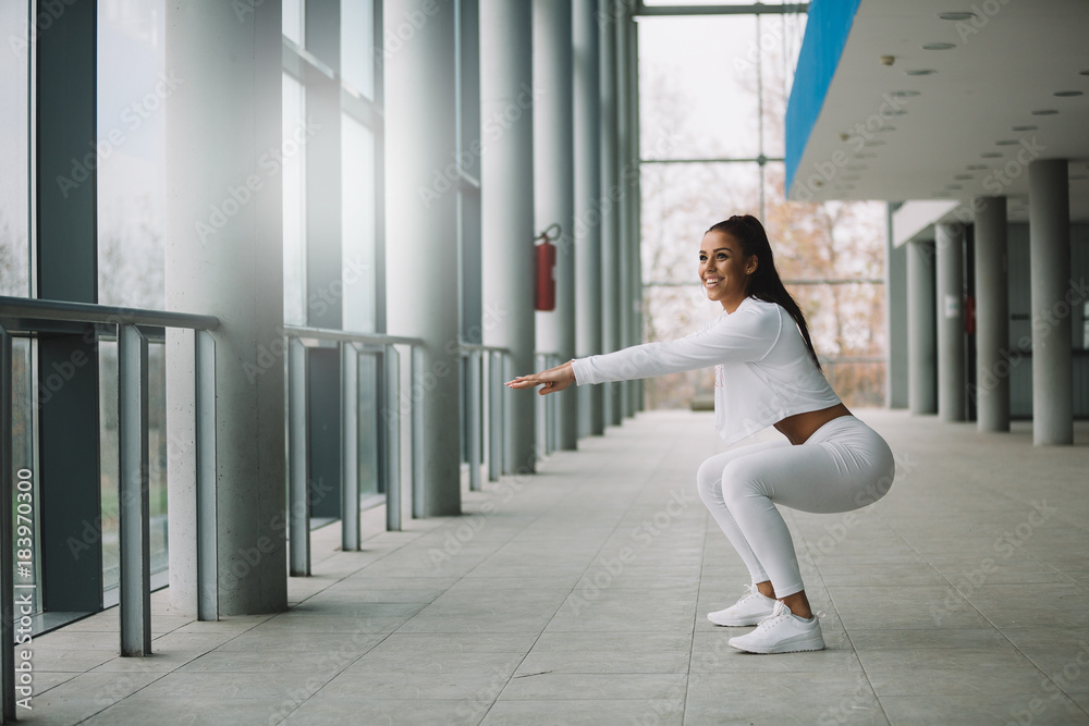 Young fit sporty girl dressed in white doing squat.