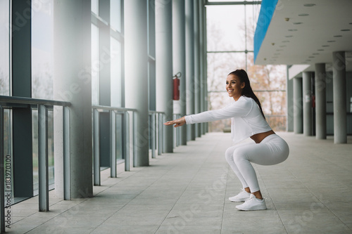 Young fit sporty girl dressed in white doing squat.