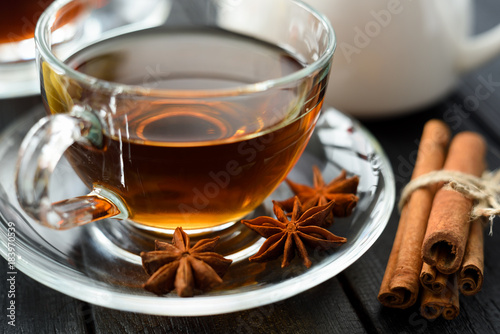 Hot spiced tea with cinnamon and star anise in glass cup on black background