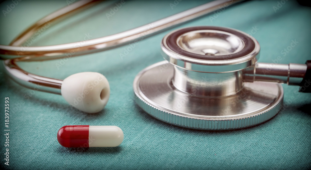 Red and white capsule next to a stethoscope, conceptual image Red and white capsule next to a stethoscope, conceptual image
