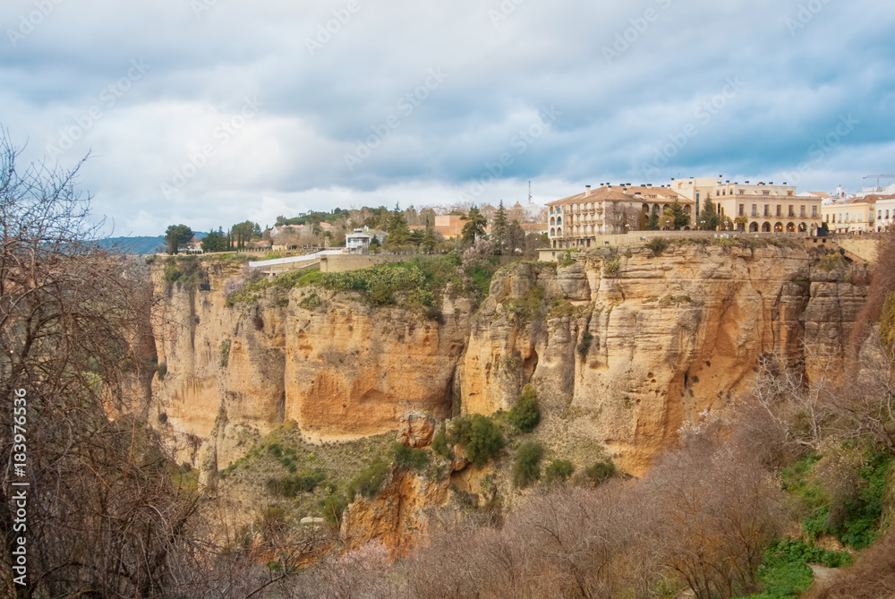 A view to El Tajo Gorge Canyon, traditional andalusian houses at the cliff and a lot of almond trees on the slope at famous white village Ronda in Malaga province, Andalusia, Spain. A view to El Tajo Gorge Canyon, traditional andalusian houses at the cliff and a lot of almond trees on the slope at famous white village Ronda in Malaga province, Andalusia, Spain.