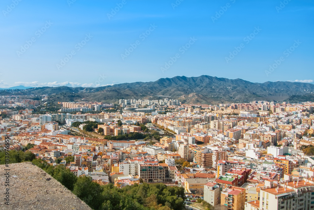 A view to the city center of Malaga and its surroundings with mountains at the background from old medieval walls of the Gibralfaro Castle of Malaga, Andalusia, Spain, on sunny evening.