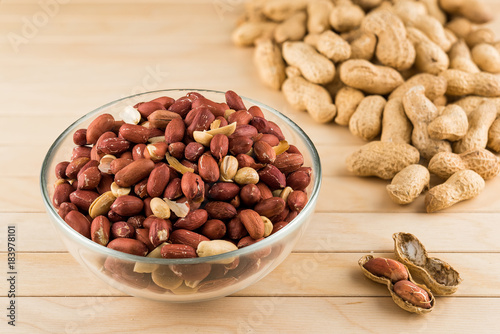 Glass bowl full of peeled peanuts and peanuts in nutshell on a wooden table