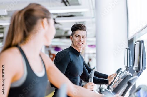 Handsome man and beautiful young woman using a stepper in a gym