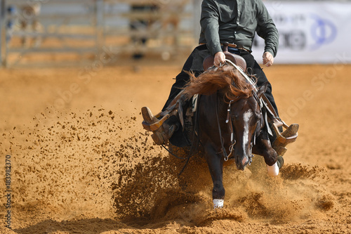 The front view of a rider in cowboy chaps and boots sliding the horse into the sand