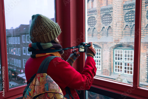 Young woman with a camera and a backpack takes pictures of European architecture in winter. Travel and photography.