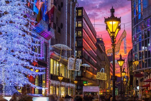Budapest, Hungary - Glowing Christmas tree and tourists on the busy Vaci street, the famous shopping street of Budapest at Christmas time with shops and beautiful sunset sky photo