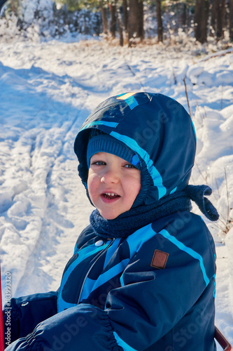 close-up portrait of a young beautiful blue-eyed boy playing in the snow while walking in a winter snowy forest park