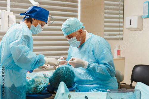 Male old professional dentist surgeon in uniform and female assistant helps to performing operation install dental implant teeth of woman patient in clinic light office with modern tools equipment. photo