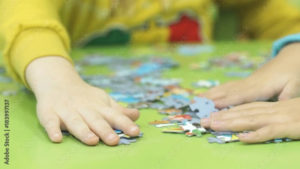Close-up of hands of little unidentified child collecting picture from puzzles at the table in kindergarten