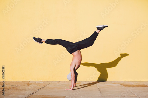 Man breakdancing in front of a yellow wall.