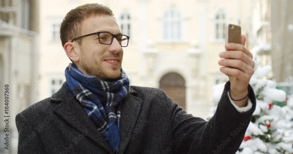 Portrait shot of the caucasian man having video chat in the street of the city center decorated for the Christmas on the snowy winter day. Outdoor Portrait shot of the caucasian man having video chat in the street of the city center decorated for the Christmas on the snowy winter day. Outdoor