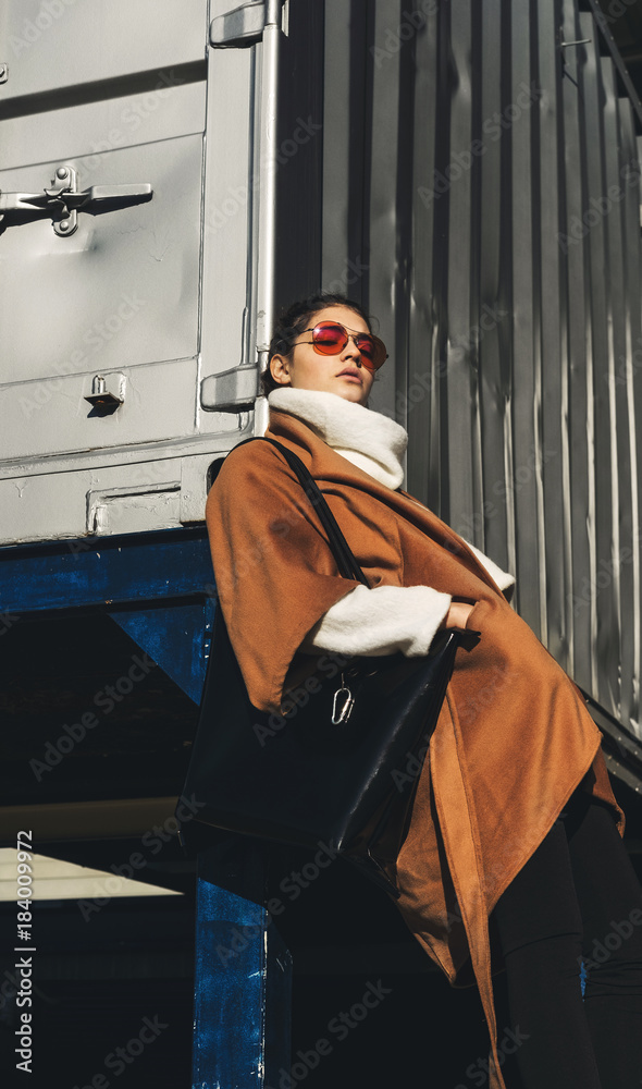 Fashionable portrait of stylish young female in brown coat with sunglasses Fashionable portrait of stylish young female in brown coat with sunglasses