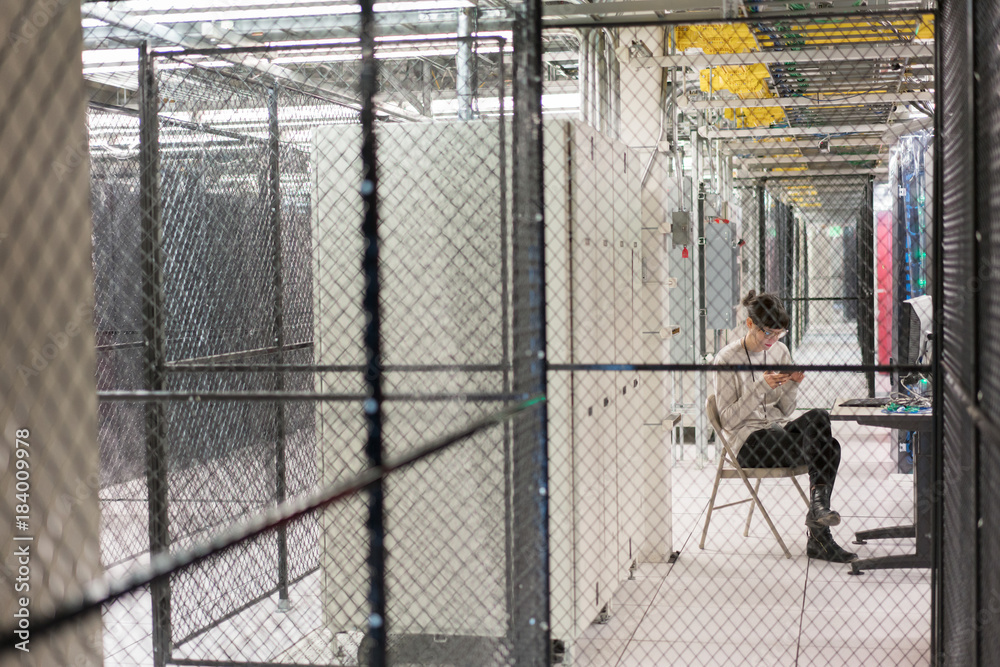 Server room technician sits in a server security cage looking at Server room technician sits in a server security cage looking at