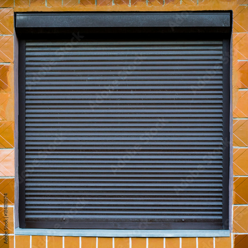 The texture of the window with blinds on the wall with ceramic tiles. Can be used as a background in interior design. Exterior of the facade of the house. Metal roller shutter for shop