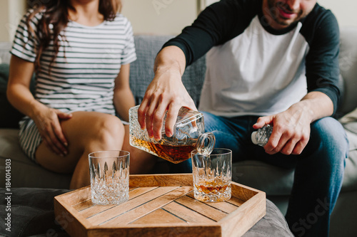 A man and woman sitting on the couch. Pour scotch / whiskey on glasses