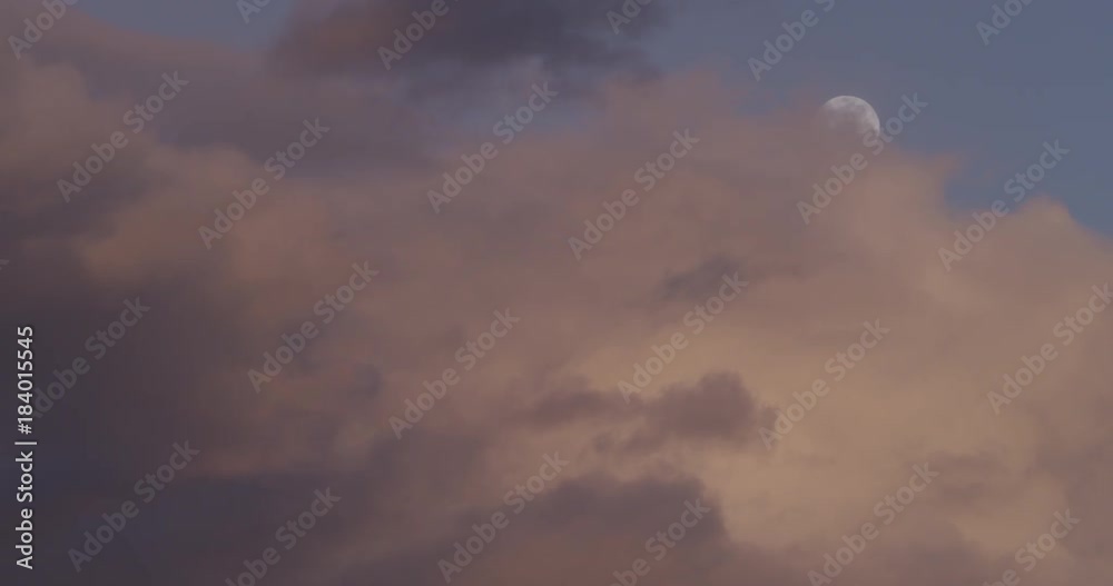 Low angle, pan right of clouds over moon at sunset