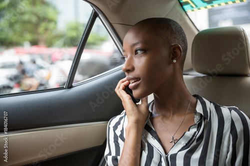 Portrait of happy young African American woman sitting in car talking on cellphone