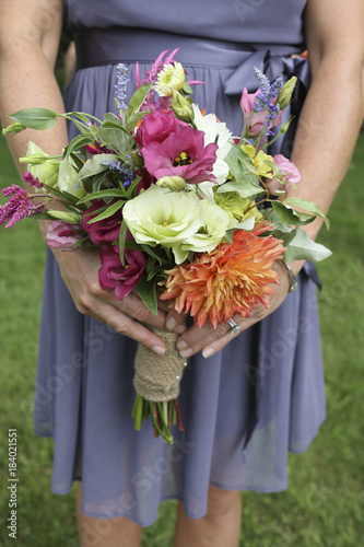 Bridesmaid in a Purple Dress holding a Bouquet of White, Green, Yellow, Orange, and Magenta Flowers Wrapped in Burlap