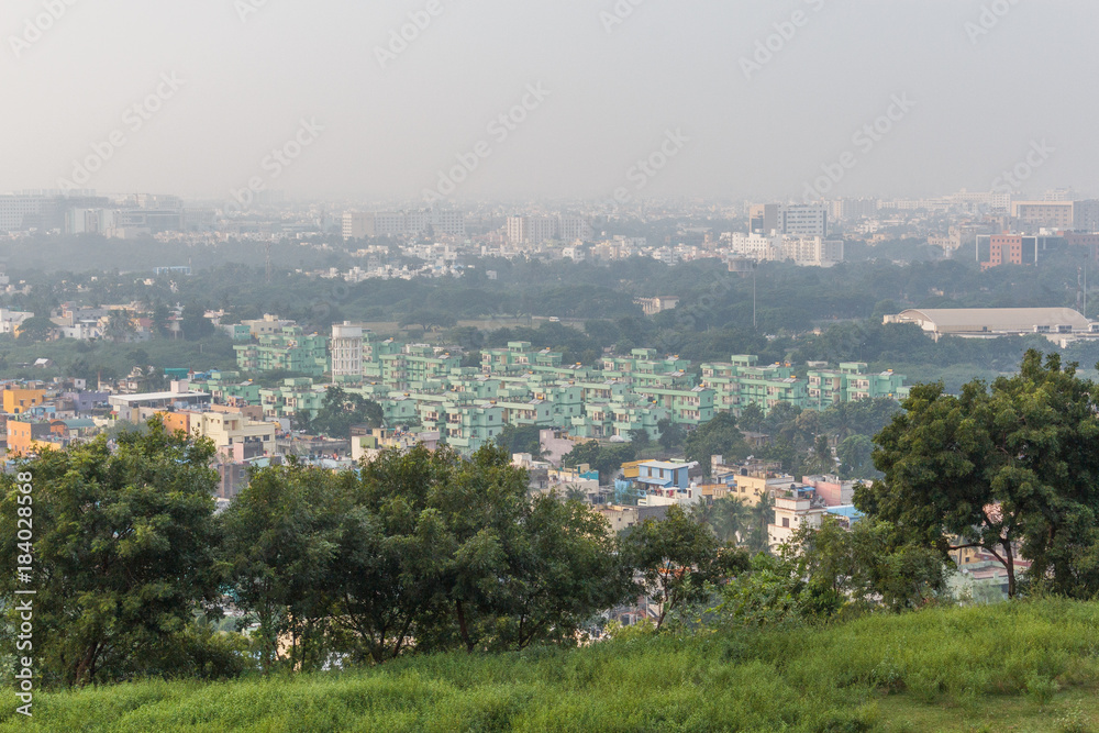 Breathing view of Chennai city landscape seen with resident buildings in the background and trees in the foreground covered by thick smoke or fog
