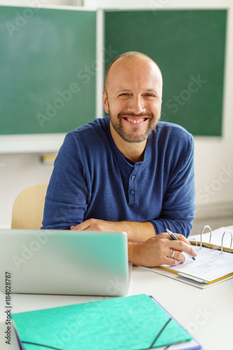 lächelnder lehrer sitzt am tisch im klassenzimmer photo