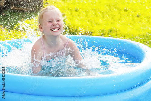 Little blonde girl playing in outdoor swimming pool on hot summer day.