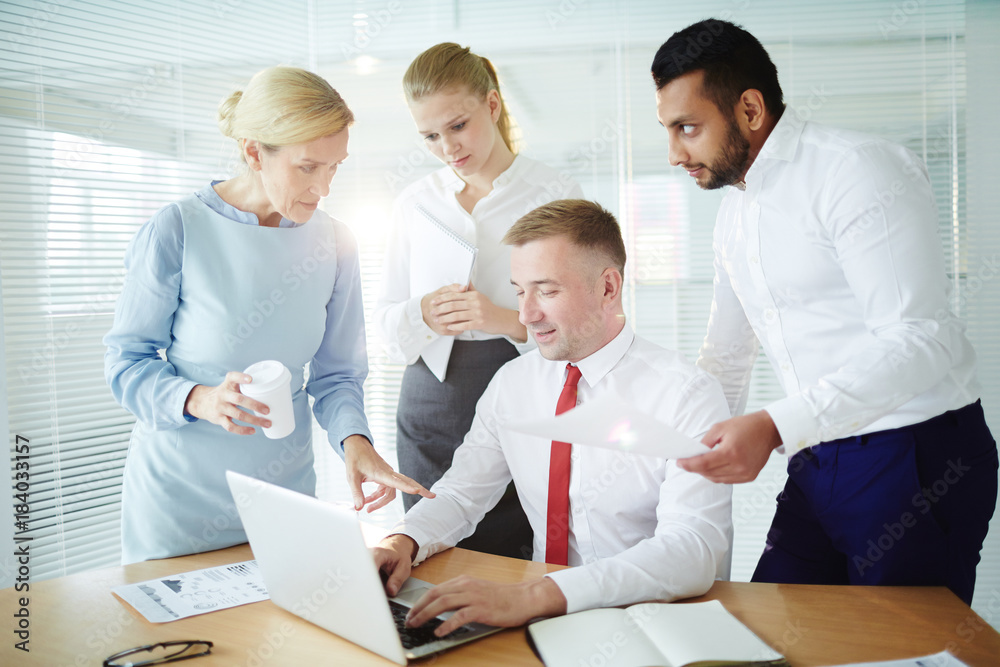 Group of confident co-workers having discussion of new project and searching for online data Group of confident co-workers having discussion of new project and searching for online data