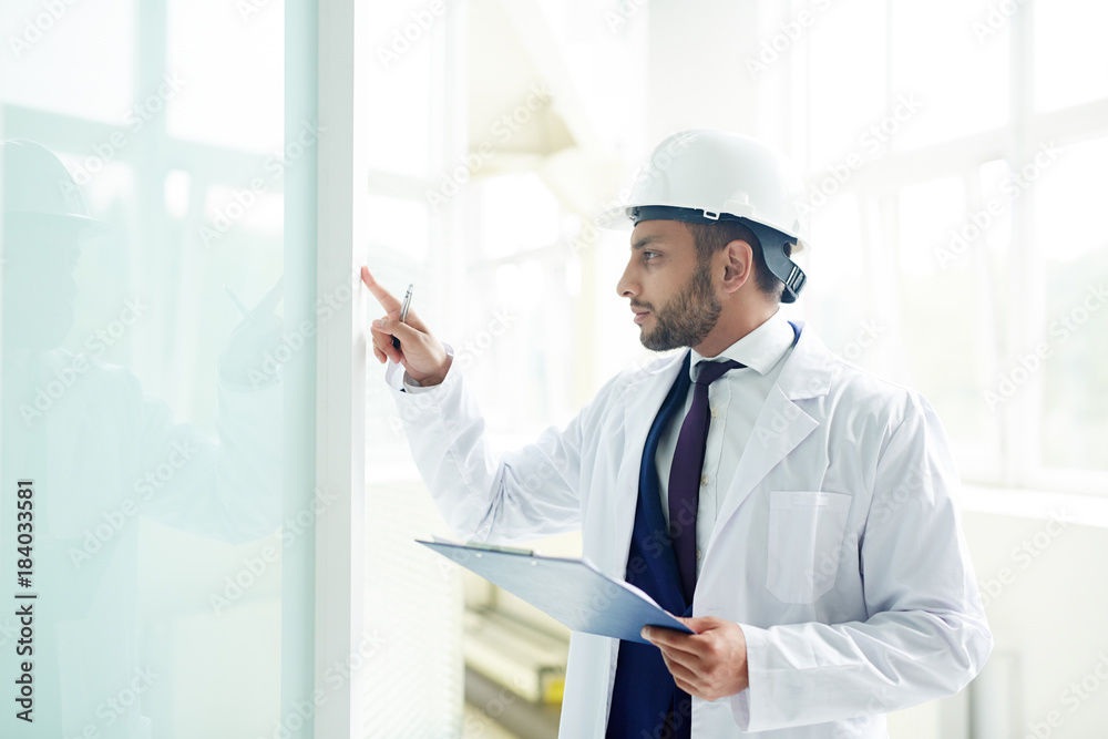 Young investor in protective helmet and whitecoat checking quality of new office-center interior Young investor in protective helmet and whitecoat checking quality of new office-center interior