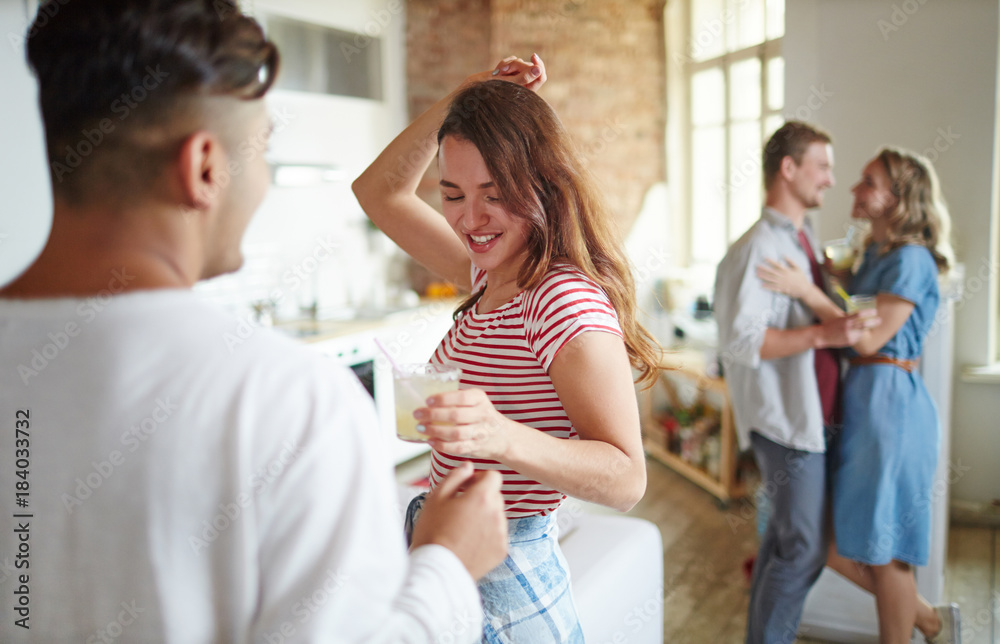 Hapy girl with cocktail dancing by her boyfriend at party with their friends on background Hapy girl with cocktail dancing by her boyfriend at party with their friends on background