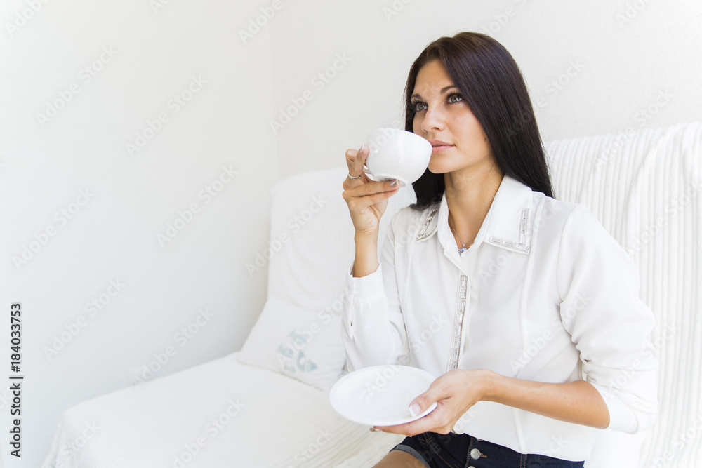 Beautiful stunning woman sipping coffee from a white cup