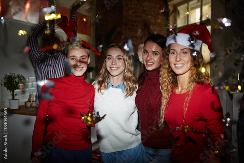 Company of affectionate girls in sweaters embracing on background of ecstatic friends