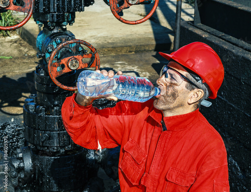 Oil Worker Drinks Water Beside Oil Well photo