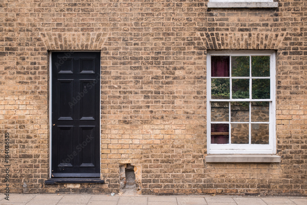 Black front door on a restored brick wall of a Victorian house residential building with white wooden sash window