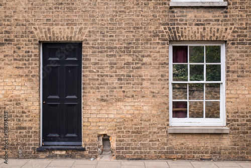 Black front door on a restored brick wall of a Victorian house residential building with white wooden sash window