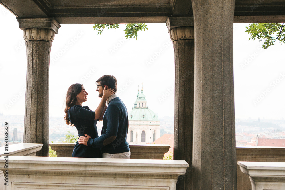 A loving young beautiful couple of students from Europe embrace and communicate at the observation deck in Prague next to the columns. Close feelings and emotions between people.