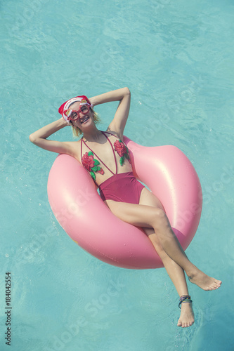Young woman in christmas hat and swimsuit celebrating new year or christmas in pool. Tropical winter vacation concept