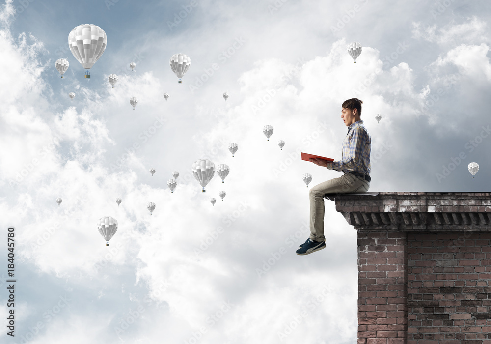 Man on roof edge reading book and aerostats flying in sky Man on roof edge reading book and aerostats flying in sky