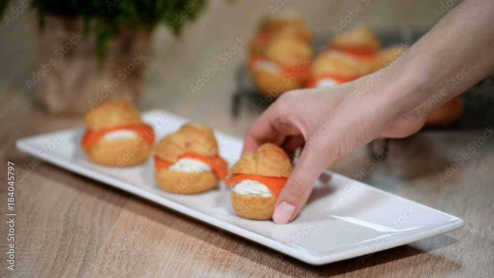 Female hands put profiteroles with salmon in a white plate Female hands put profiteroles with salmon in a white plate