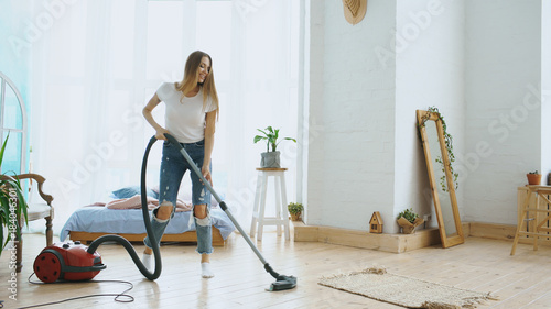 Young woman having fun cleaning house with vacuum cleaner dancing and singing at home photo